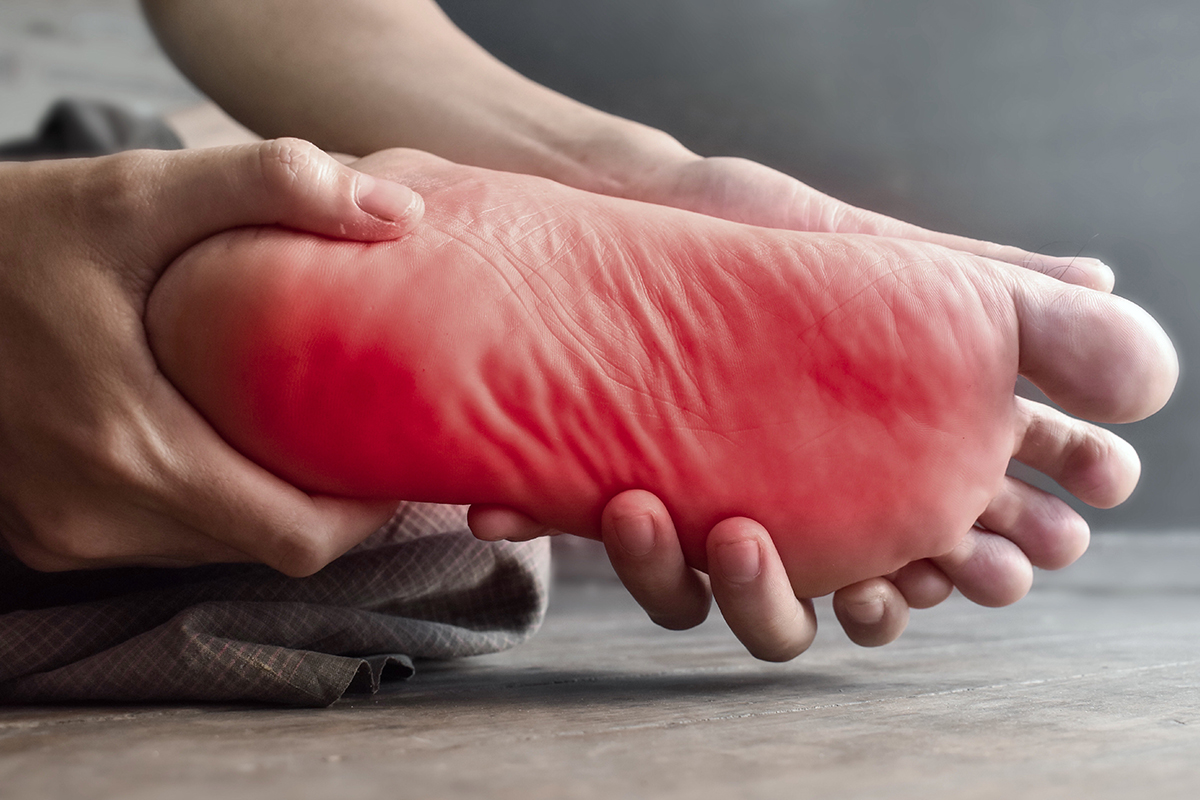 A person holding their foot which is bright red indicates the pain that can be felt in the feet from Neuropathy. Maumee Integrated Health can help resolve nerve pain with our Neuropathy Treatment.